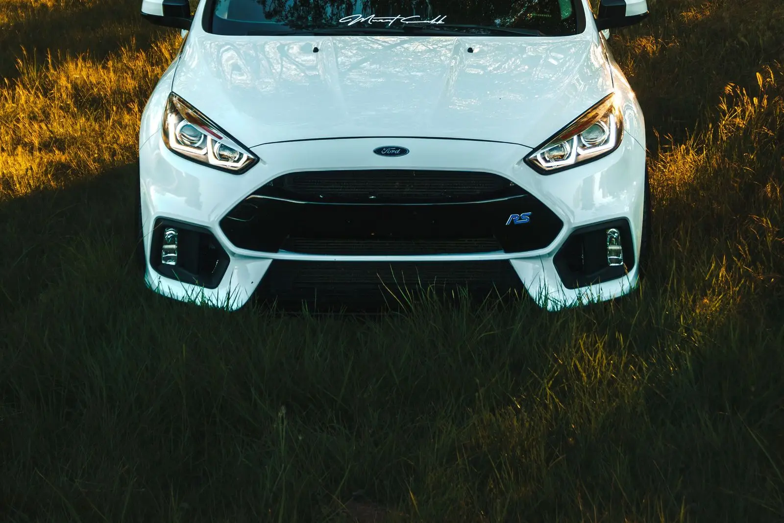 Gün batımında çimende duran beyaz hatchback, ön görünüm